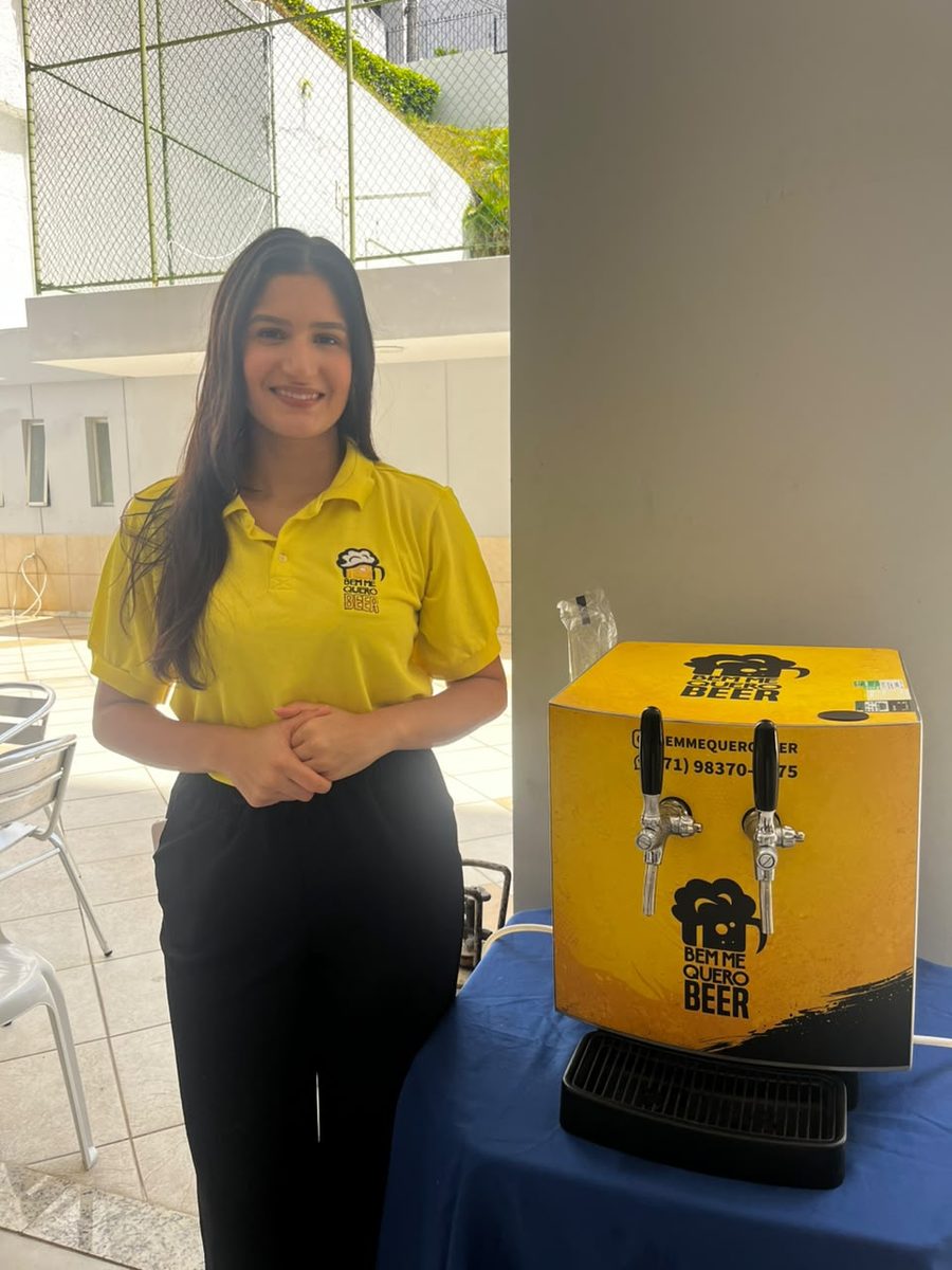 Atendente uniformizada da Bem Me Quero Beer ao lado da chopeira elétrica de 2 vias